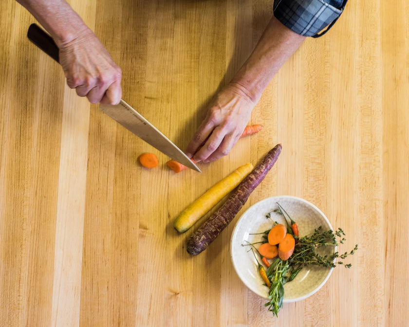 Person cutting carrots on a wooden cutting board with a bowl of chopped vegetables nearby.
