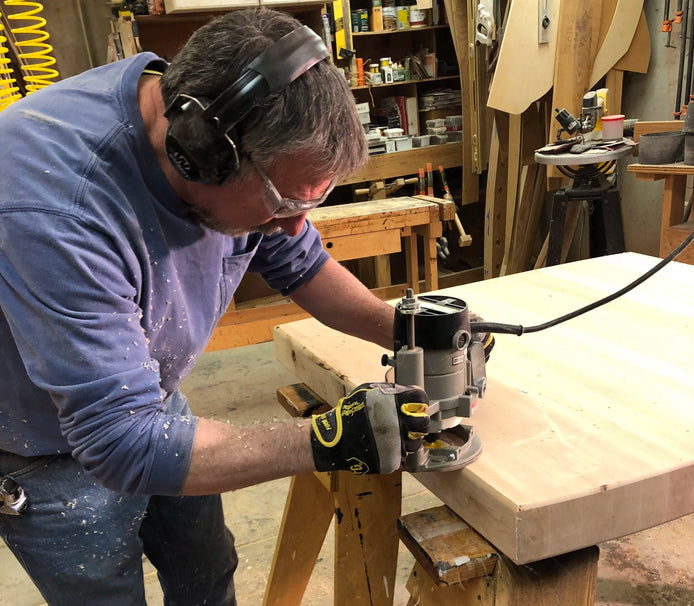 Man using a router on a piece of wood in a workshop.