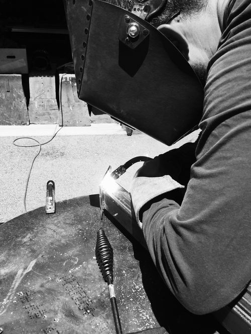 Person welding metal with a torch, wearing protective gear.